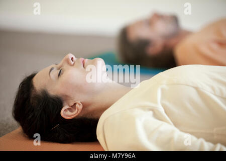 Two young people practising relaxation also called yoga nidra. Laying in shavasana on their backs, on their yoga mats in yoga class indoor in loose li Stock Photo