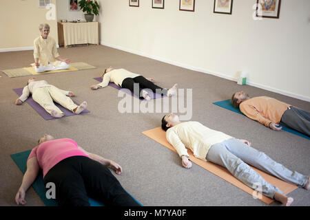 Young people practising relaxation also called yoga nidra. Guided by a certified female yoga instructor laying in shavasana on theri backs on yoga mat Stock Photo