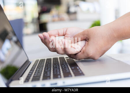 Close up woman holding and pressing or touching her hand while working with laptop in the office. Numbness or pain on hand concept. Stock Photo
