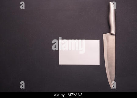 New stainless steel cooking knife on black stone background. Top view with free space and paper note for text or design Stock Photo