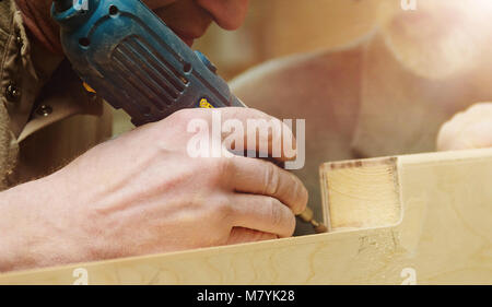 Closeup of Carpenter in Cap and Pullover Sanding Plank in Workshop. Industrial Manufactoring Concept. Stock Photo