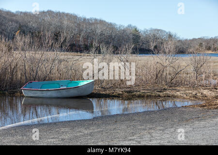 a small colorful row boat sitting in shallow water, having been washed ashore during a storm. Stock Photo