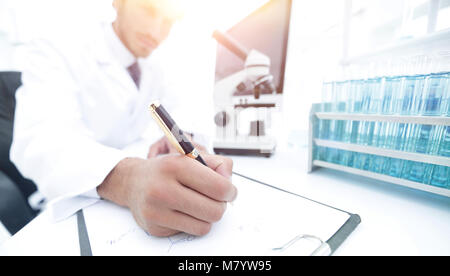 A young male lab specialist is working on some samples and takes notes in his clipboard Stock Photo