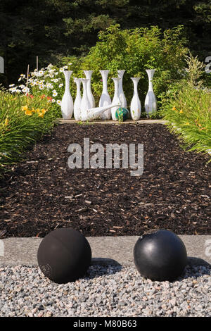 Black bowling balls and mulch alley with concrete bowling pins in a landscaped residential backyard garden in summer. Stock Photo