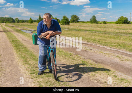Senior with green suitcase getting ready to ride on a bicycle on a country road Stock Photo