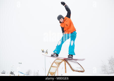 Picture of young sporty man with his hand raised skiing on snowboard in springboard background of snowy sky in winter Stock Photo
