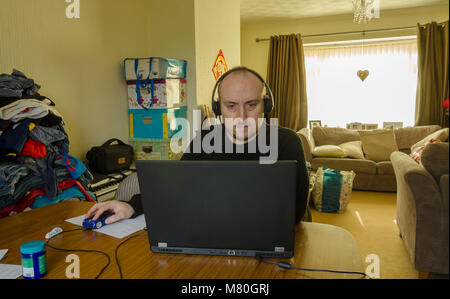 A middle aged man working from home on a laptop computer on the dining room table. Stock Photo