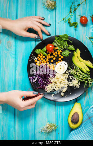 Woman hands and Healthy vegan lunch bowl. Vegan buddha bowl. Vegetables and nuts in buddha bowl on blue wood background. Top view Stock Photo