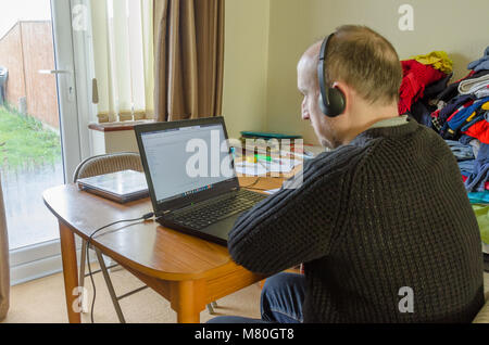 A middle aged man working from home on a laptop computer on the dining room table. Stock Photo