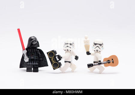 Lego Darth vader holding light saber watching storm troopers holding a radio and a guitar. isolated on white background. Stock Photo