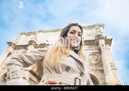 Low angle view of young pretty tourist woman smiling looking at camera, in background arch of Constantine monument in Rome Italy Stock Photo