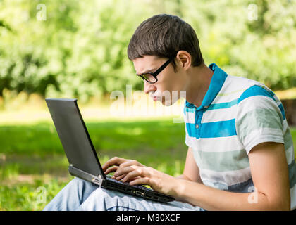 Student at work on laptop sitting under tree Stock Photo