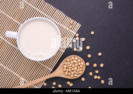 Soy milk in white cup and soy bean on dark table background. Top view Stock Photo