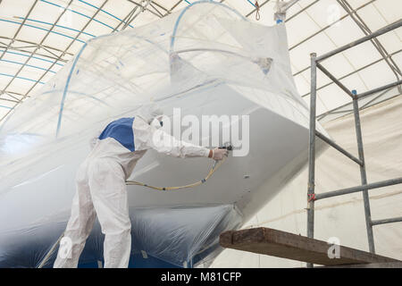 Worker wearing protective uniform and spraying paint to the boat, Maintenance concept Stock Photo