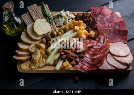 Assorted from meat and cheese on a chopping board. Smoked sausage, meat roll from a turkey with cheese, jamon, olives, nuts and various grades of cheese. Mediterranean traditional snack. Stock Photo