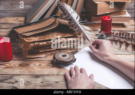 The female hand writes the letter with feather quill pen. Old books, compass on a wooden background. Retro style Stock Photo