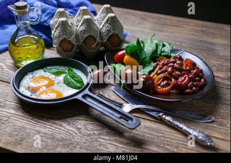 The pan fried eggs, haricot stewed in tomato sauce and fresh spinach. Concept of a healthy breakfast. Stock Photo