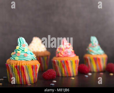 home baked cupcakes with colorful frosting and fruit on a stone table Stock Photo
