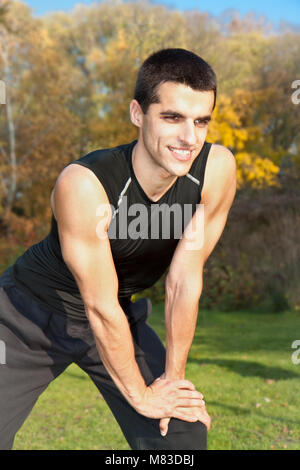 Attractive young man doing exercise in autumn park Stock Photo
