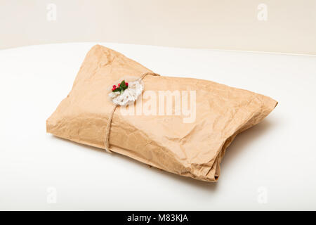 Gift in crumpled wrinkled brown paper tied with string and attached decoration with red berries on a white background Stock Photo