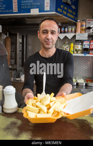 Man serving chips at a takeaway fish and chips restaurant Stock Photo