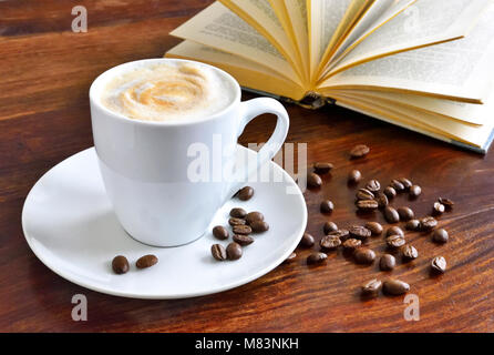 Breakfast scene with coffee cup, open book and coffee beans on a wooden table. Morning scene with hot coffee.