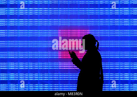 Silhouette of woman using her smartphone in front of  blue / red LED wall Stock Photo