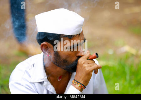 Man in white cap wearing a white shirt smoking, side profile. Pandharpur festival Stock Photo
