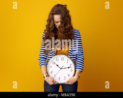 stressed trendy woman in striped jacket against yellow background with clock Stock Photo