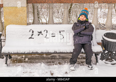 Naughty boy wrongly decides an example on a snow-covered bench Stock Photo