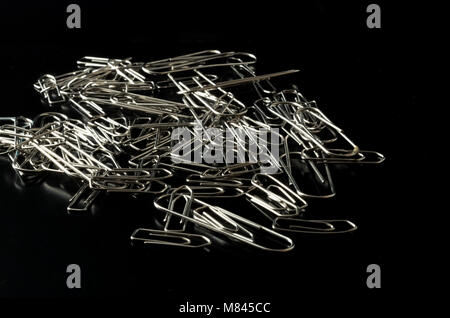Pile of metal paper clips on reflective black background Stock Photo