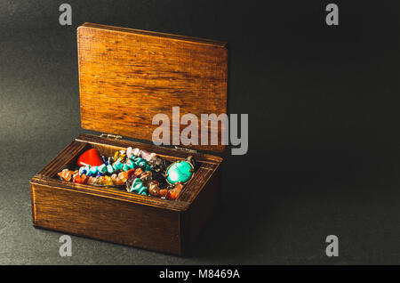 Wooden box full of colorful jewelry on dark grey background Stock Photo