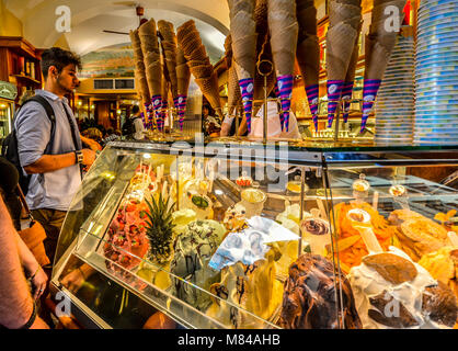A young man orders gelato at a colorful gelateria with many flavors and waffle cones in Florence Italy Stock Photo