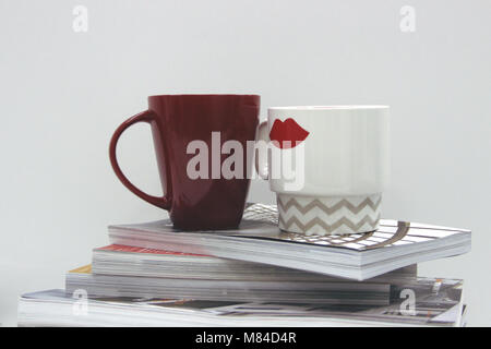 Red/white office photo of coffee cups on top of pile of thick magazines for entrouage of editor's worplace or similar Stock Photo