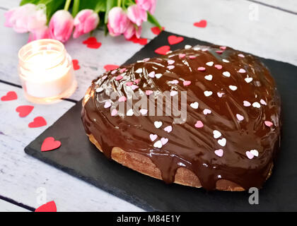 Birthday cake or chocolate cake with confetti and burning candle. Wooden table with heart shaped cake and chocolate topping, Valentines Day. Stock Photo