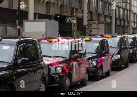 Parked London black cab taxis awaiting a fare near Kings Cross Station with taxi light illuminated. Stock Photo