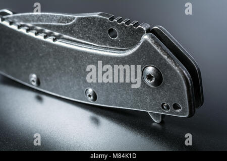 Macro Of A Standing Handle Of A Black Closed Folding Knife With Reflection On Dark Ground Stock Photo