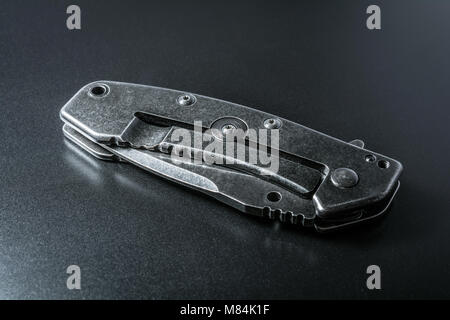 Handle Of A Closed Black Folding Knife Lying On Dark Ground With Reflection Stock Photo