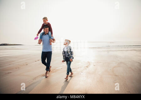 Father and his two sons walking uyp from the waters edge at the beach while on their holiday. Stock Photo
