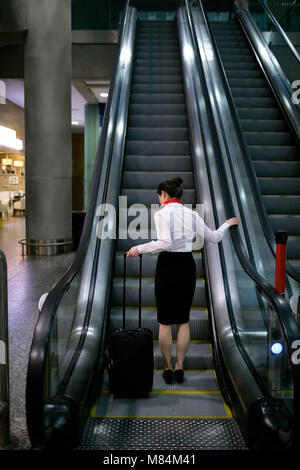 Woman standing on escalator with luggage Stock Photo