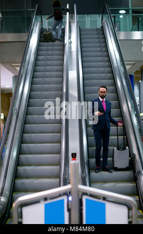 Businessman standing on escalator with luggage Stock Photo