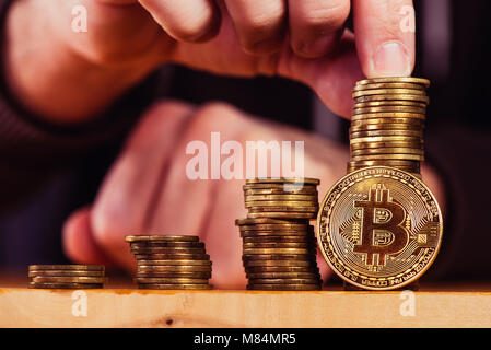 Bitcoin cryptocurrency miner stacking BTC coins, close up of male hand Stock Photo