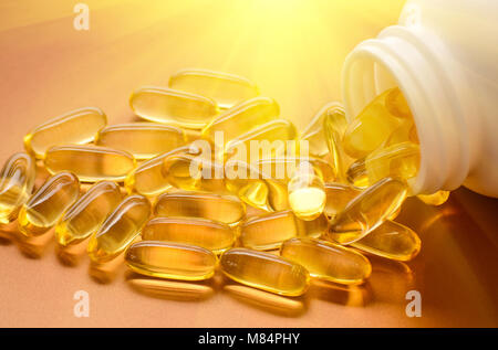 Fish oil capsules with omega 3 and vitamin D in a plastic bottle on a shiny texture with sun beams, healthy diet concept Stock Photo