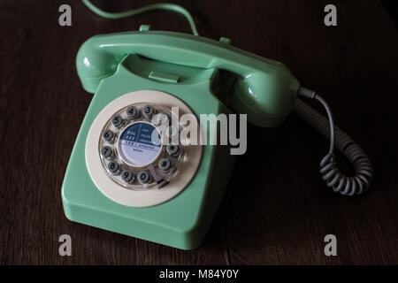 An old fashioned, vintage telephone with rotary or circular dial in a green colour and used in the seventies and eighties from British culture. Stock Photo