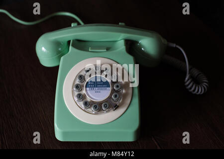 An old fashioned, vintage telephone with rotary or circular dial in a green colour and used in the seventies and eighties from British culture. Stock Photo