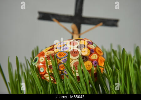 Easter Craft Ideas. The Easter egg decorated with multicolored paper,  placed between frech green wheat germs, cross and crucified in the distance, se Stock Photo