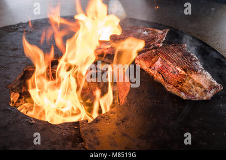 delicious steaks on a handmade bbq grill with flames rising from the charcoal underneath Stock Photo