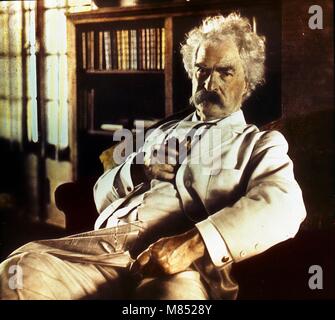Colorized portrait of American author and humorist Mark Twain, born Samuel Langhorne Clemens (1835 - 1910) holding a pipe and glasses, with a newspaper in his lap, circa 1900. (Photo by Burton Holmes) Stock Photo