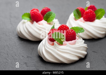 Mini  Pavlova meringue nests with raspberries and mint on black stone background Stock Photo