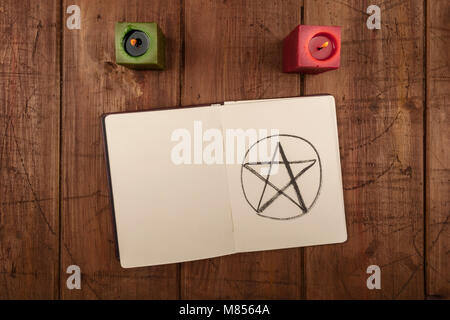 An overhead photo of two candles and an open grimoire, a witch's book of spells, with a hand-drawn pentacle, shot from above on a dark background with Stock Photo